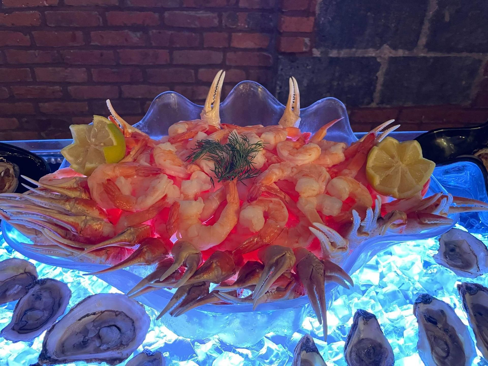A platter of shrimp and crab claws served on ice, decorated with lemon slices, surrounded by raw oysters on a bed of ice.