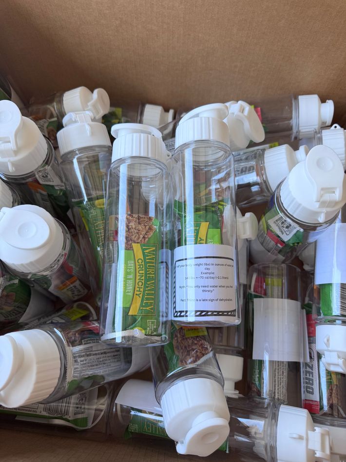 Cardboard box filled with assorted clear plastic bottles with white caps and green labels