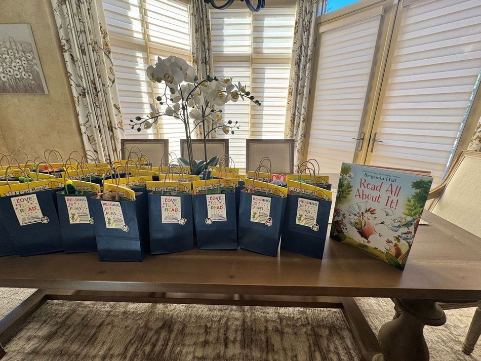 Row of blue gift bags with tags on a table beside a floral card in a bright windowed room