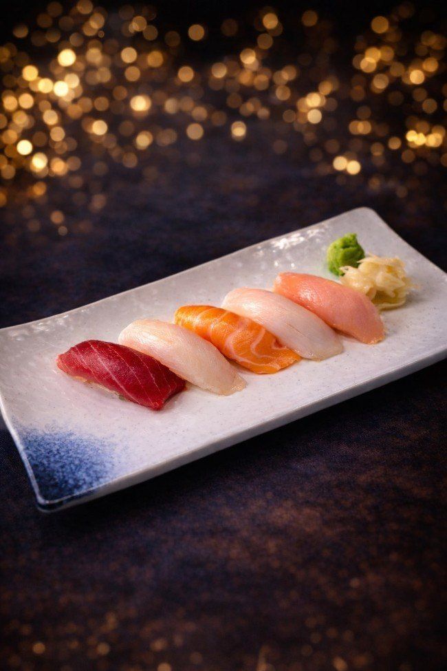 Sushi nigiri assortment on a rectangular plate, with wasabi and pickled ginger on a dark table
