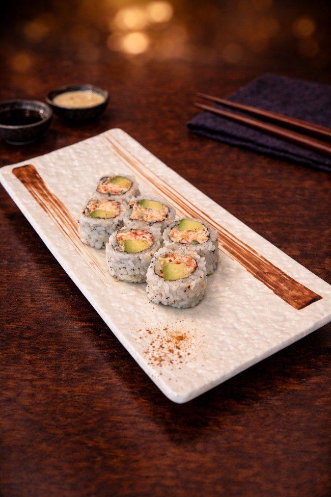 Sushi rolls on a white rectangular plate with dipping sauce on a dark wooden table.