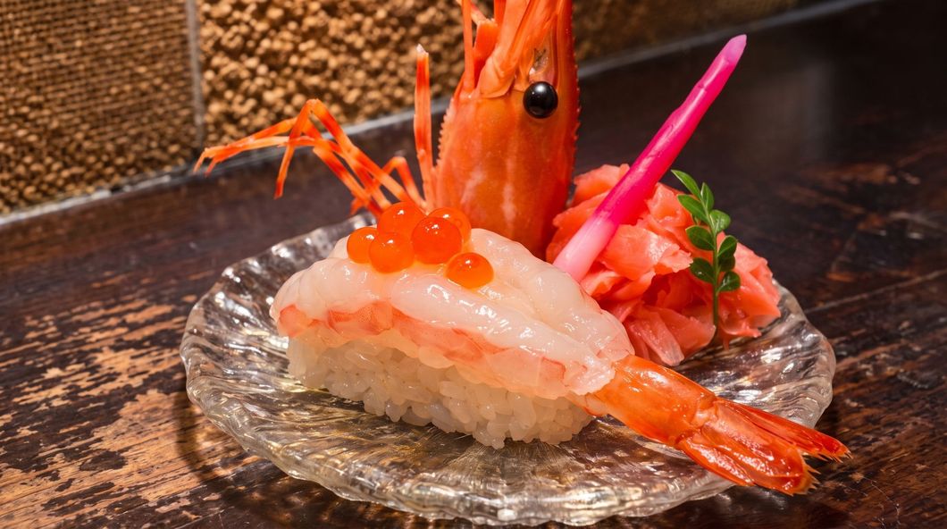 Shrimp nigiri sushi garnished with pink pickled ginger on a small glass plate