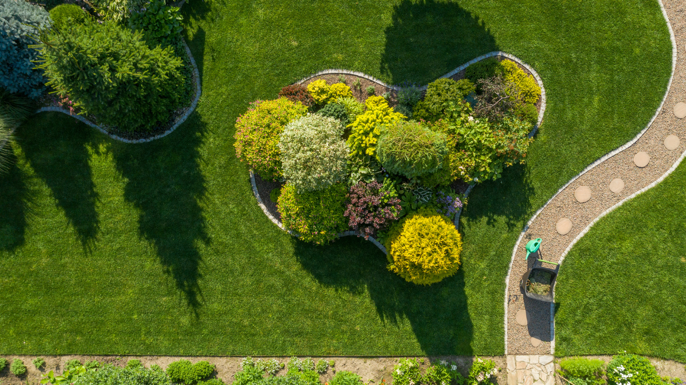 Overhead view of a well-manicured garden with a stone path, flowerbeds, and person walking.