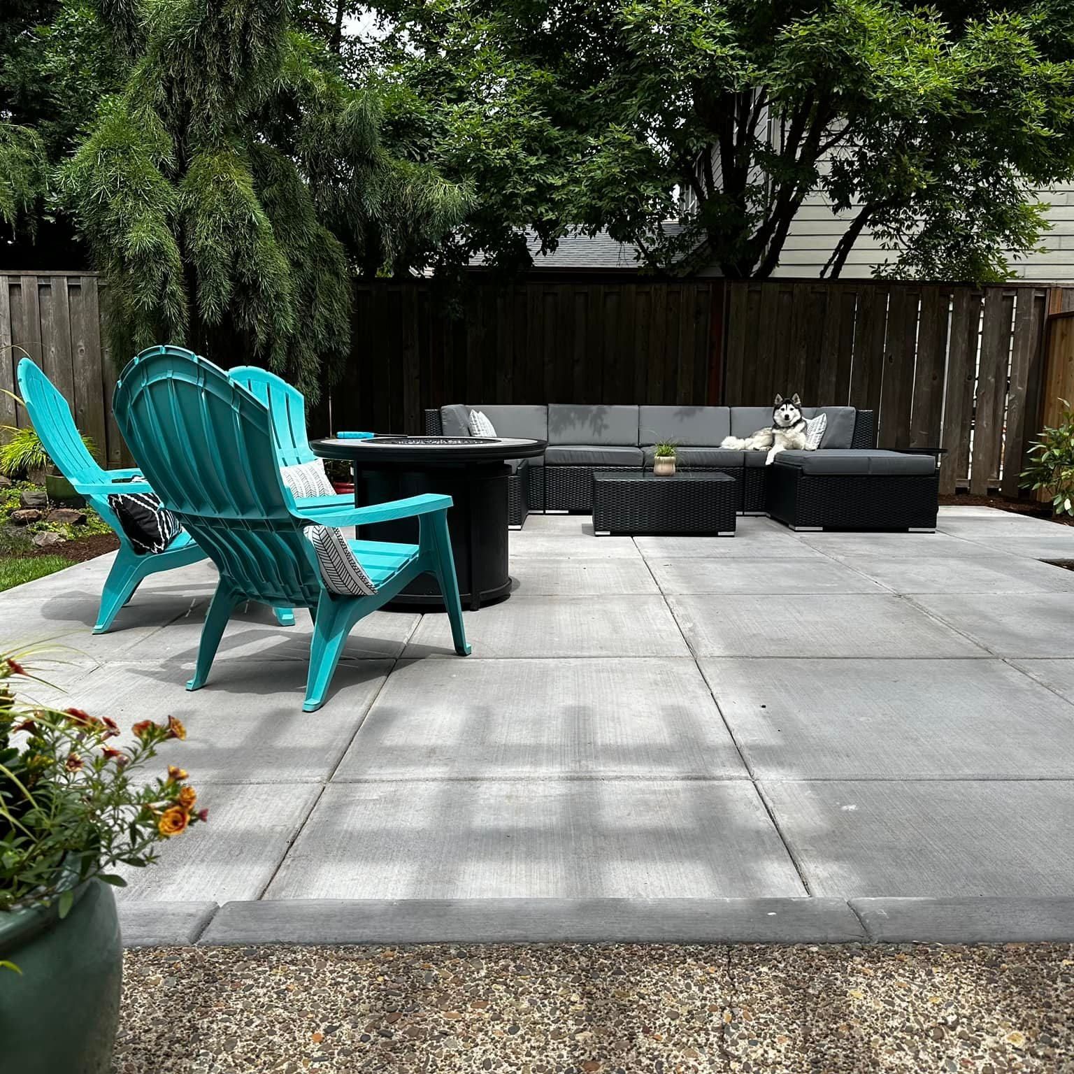 A patio with two bright turquoise Adirondack chairs, a fire pit, and a dark grey sectional sofa with a dog sitting on it.