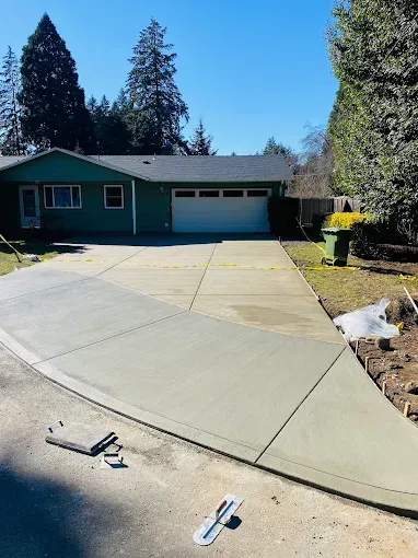 A green house with a newly poured, light grey concrete driveway extension leading to a garage on a sunny day.