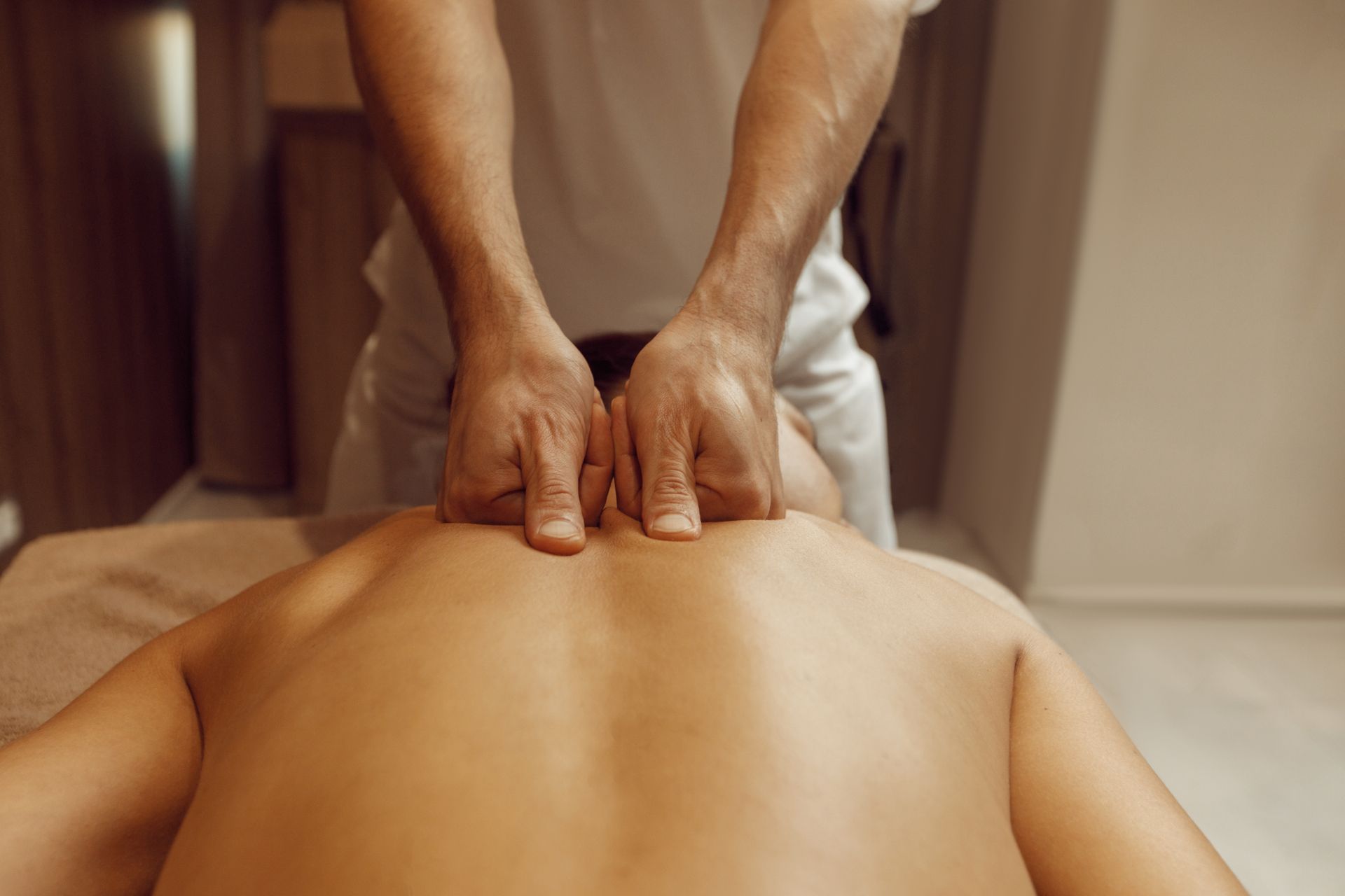 Hands massaging a person's upper back and neck on a massage table.