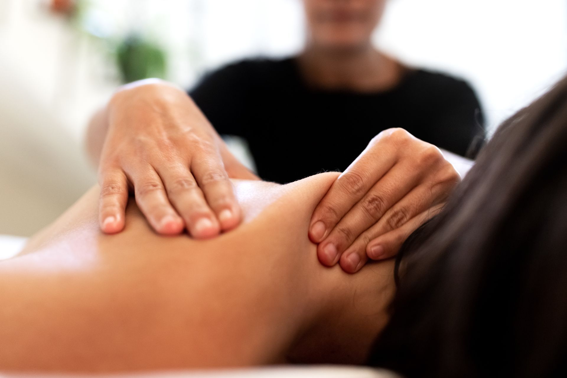 Hands massaging a person's shoulder. Another person is in the background. White setting.