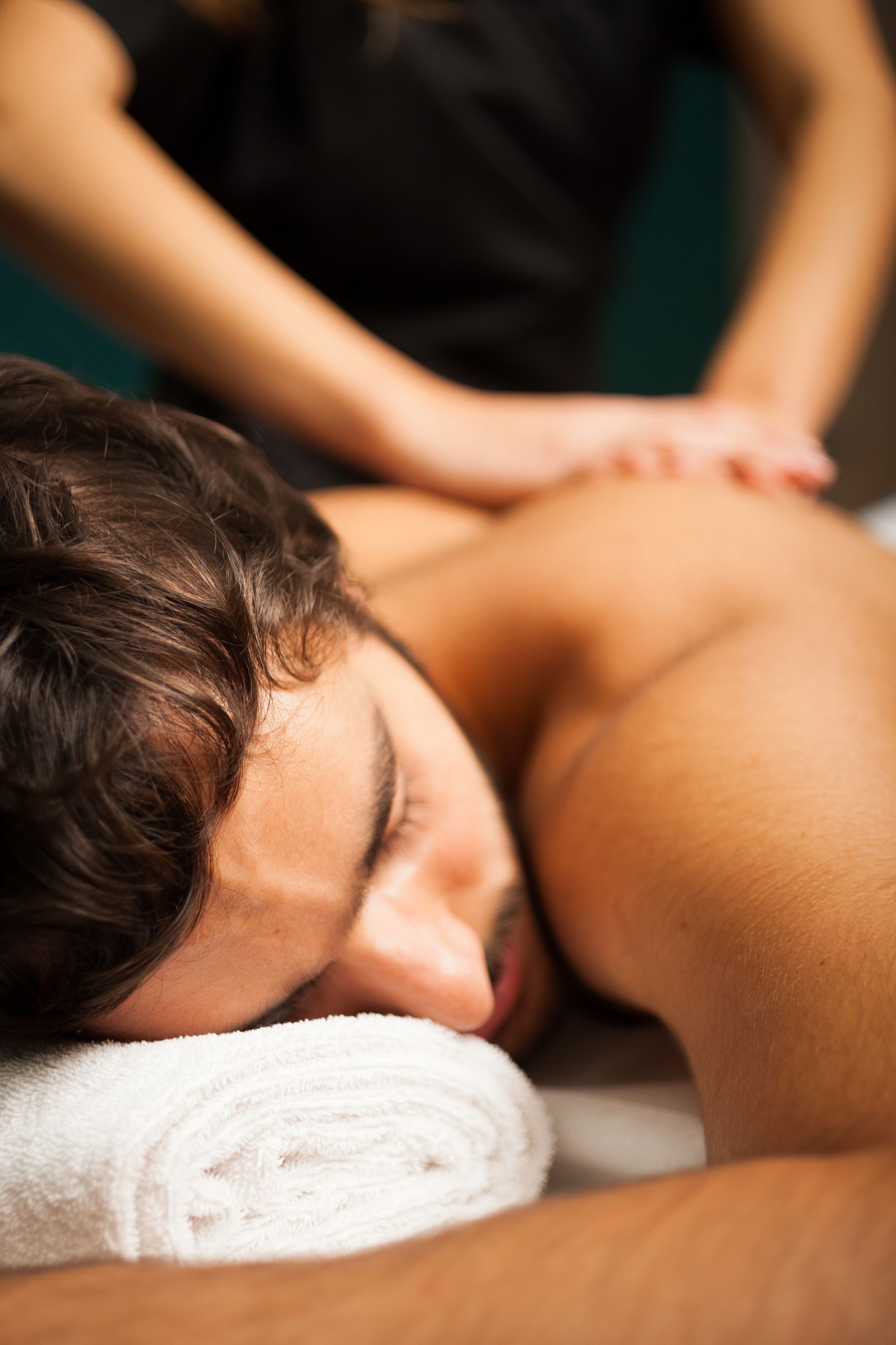 Man receiving back massage, lying face down on a towel. A therapist's hands apply pressure.