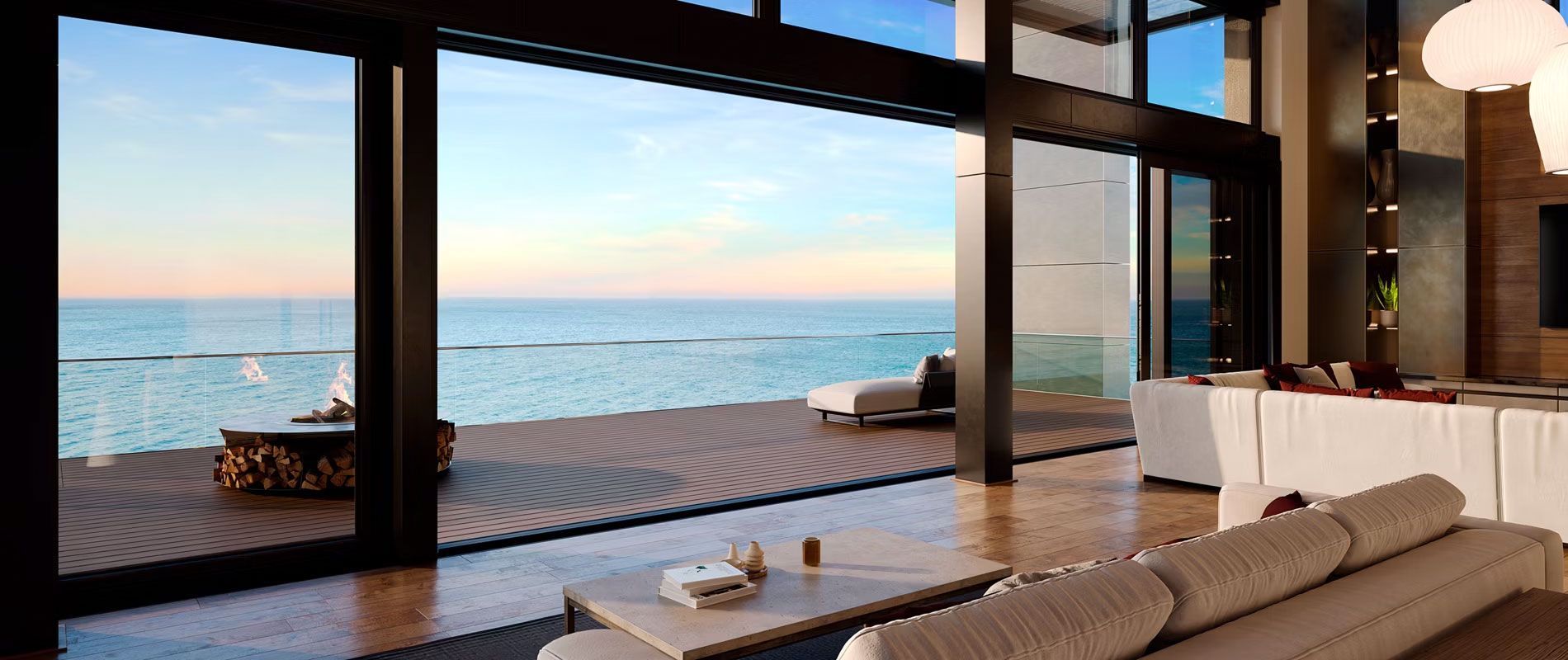A living room with a couch overlooking the composite wooden deck and a table with a view of the ocean.