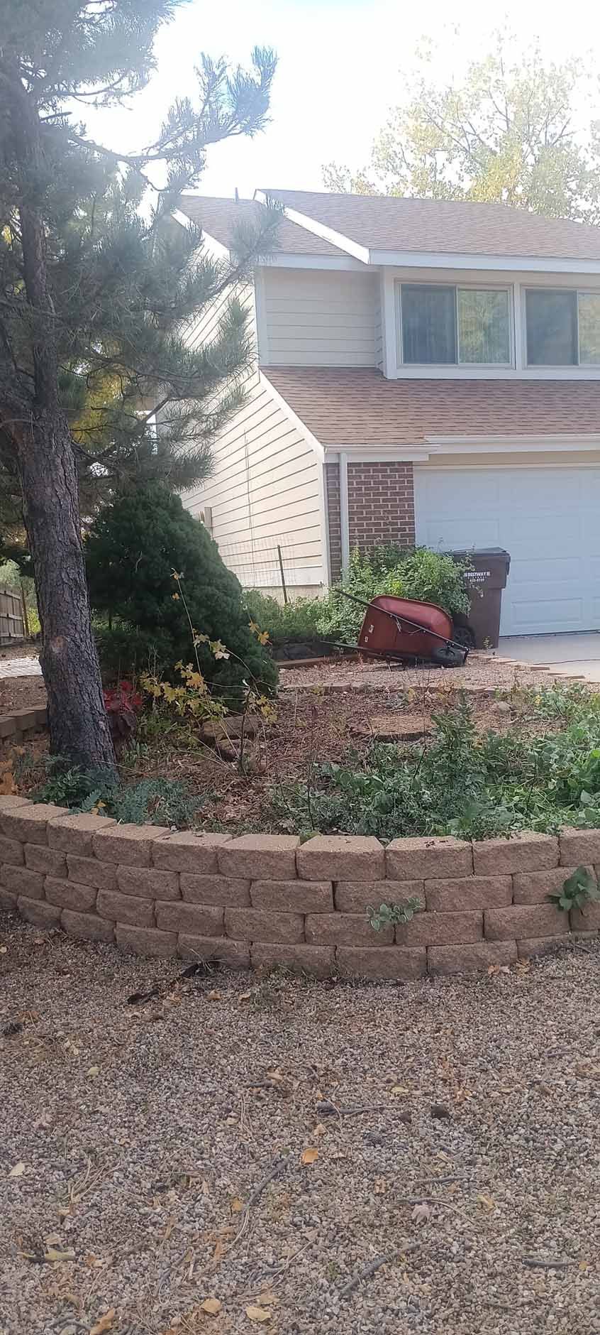 A suburban house with a tan brick wall in a front garden bed featuring a tree and gravel landscaping.