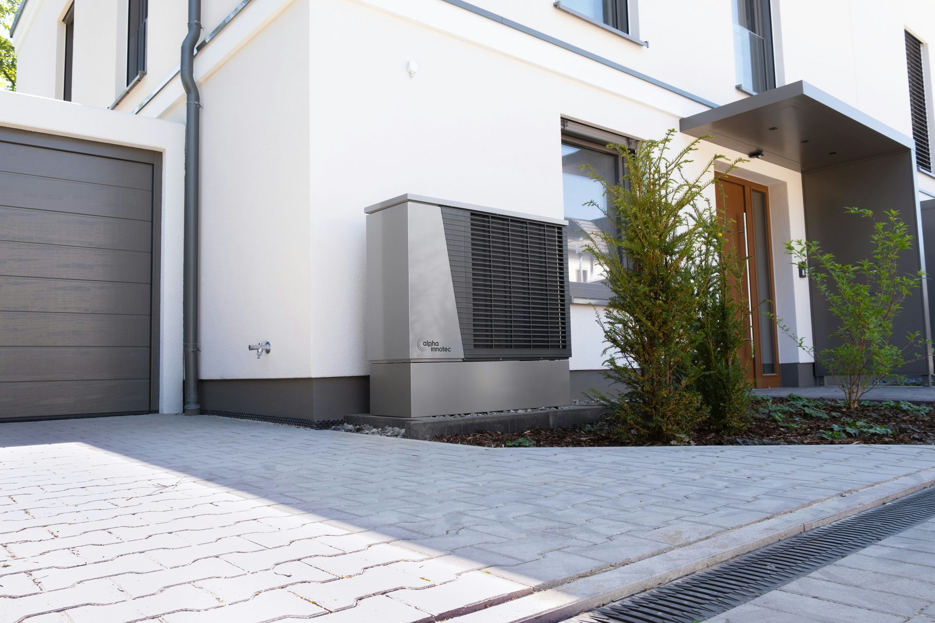 Modern house exterior with white walls, gray garage door, paved driveway, and small trees by the entrance