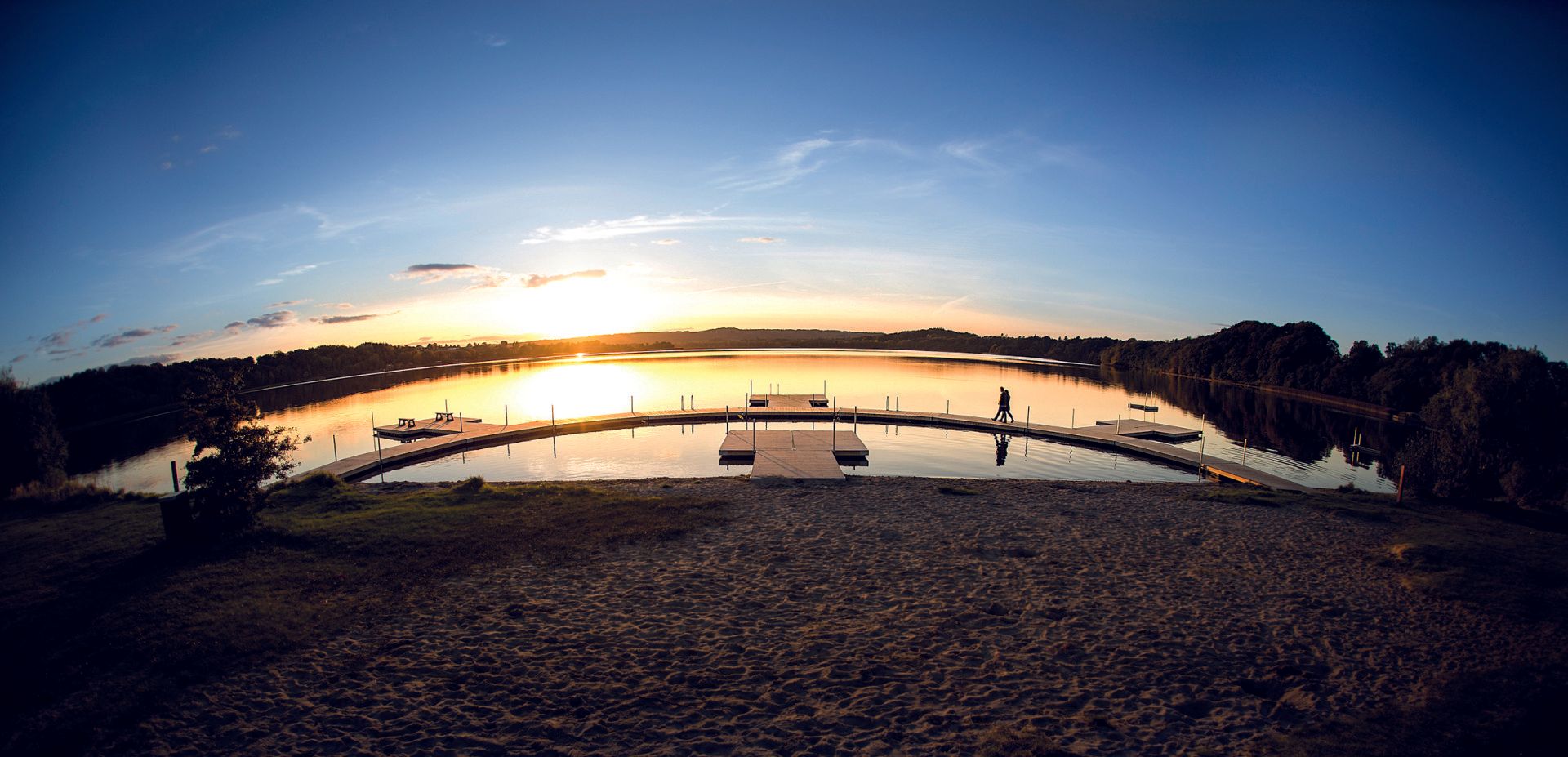 En solnedgang over en sø med en dok i forgrunden.