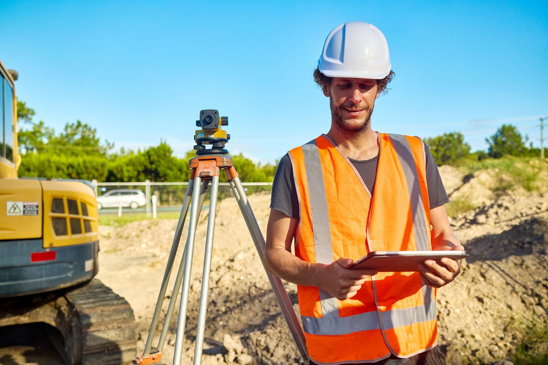 A surveyor is using a digital tablet next to a theodolite on a construction site.