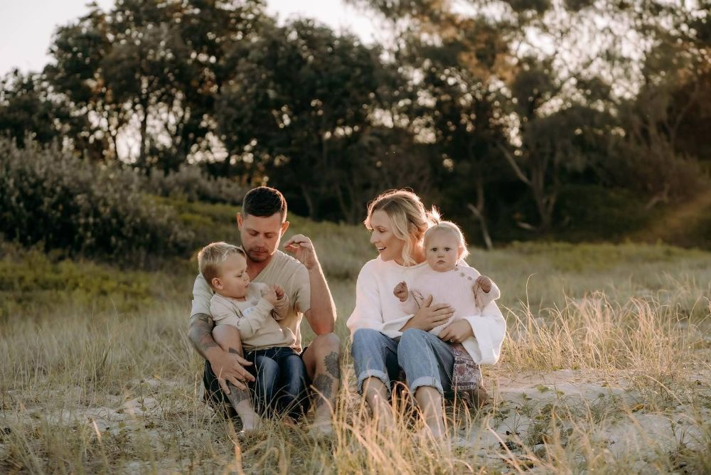 A Family Is Sitting on The Grass in A Field — Seed + Salt Photography In Coffs Harbour, NSW