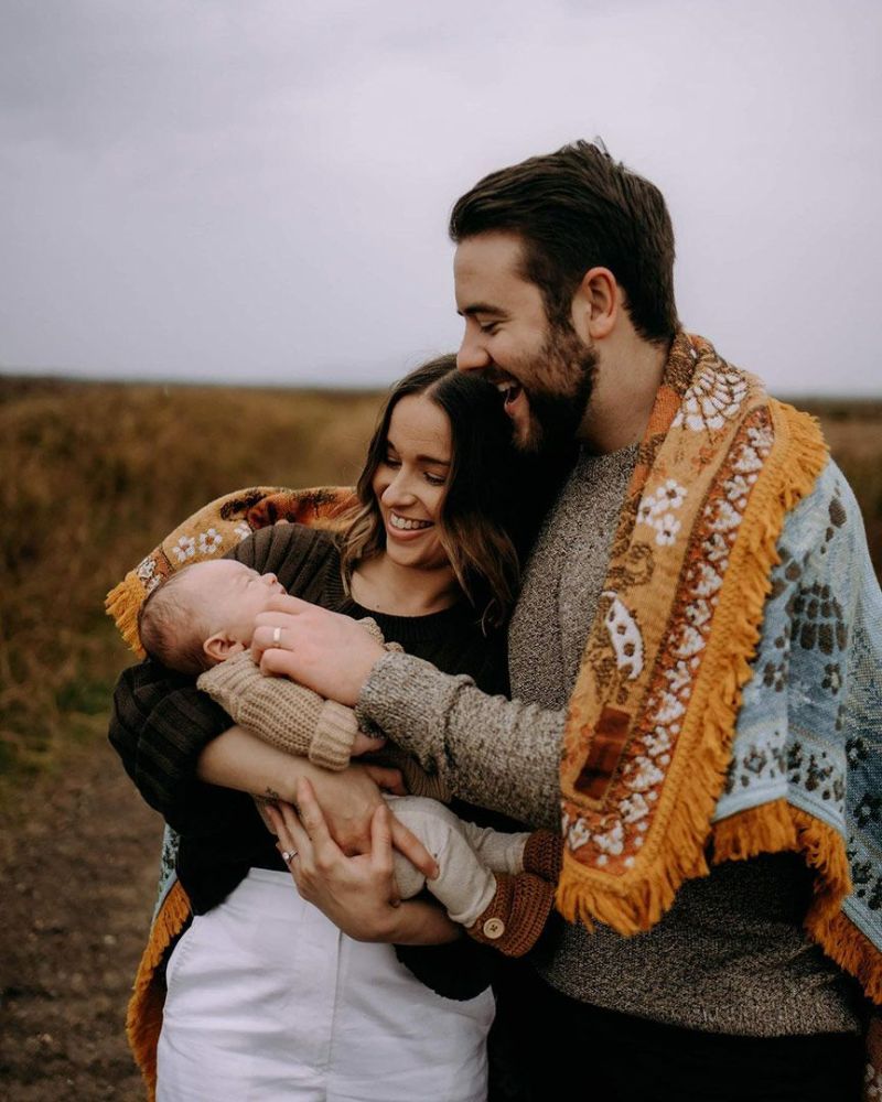 A Man and Woman Are Holding a Baby Wrapped in A Blanket — Seed + Salt Photography In Taree, NSW
