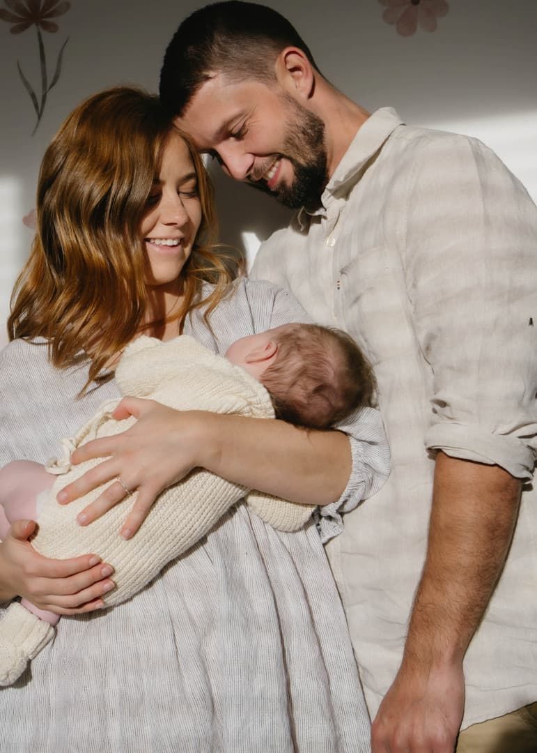 Couple Smiling Down at Their Newborn Baby Wrapped in a White Blanket โ Seed + Salt Photography In Smithtown, NSW