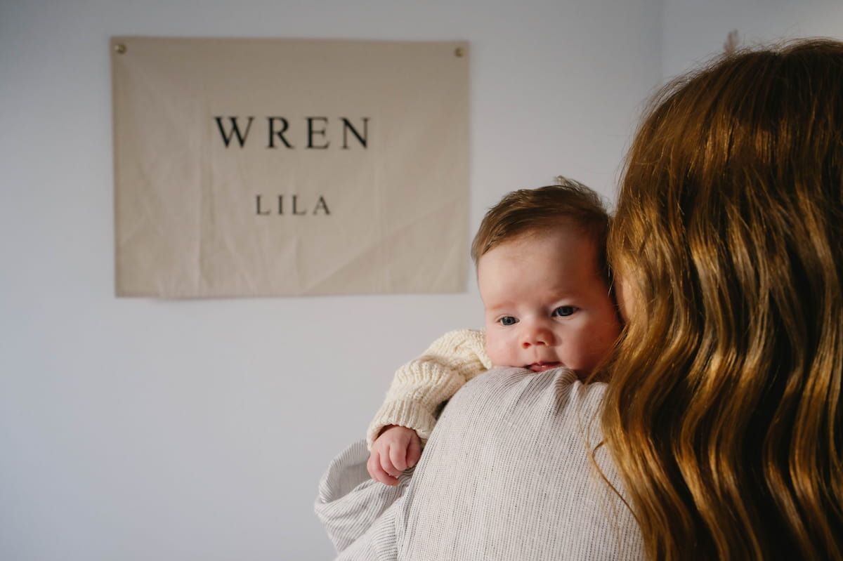 Baby Held by an Adult Beside a Wall Sign Reading โ Seed + Salt Photography In Smithtown, NSW