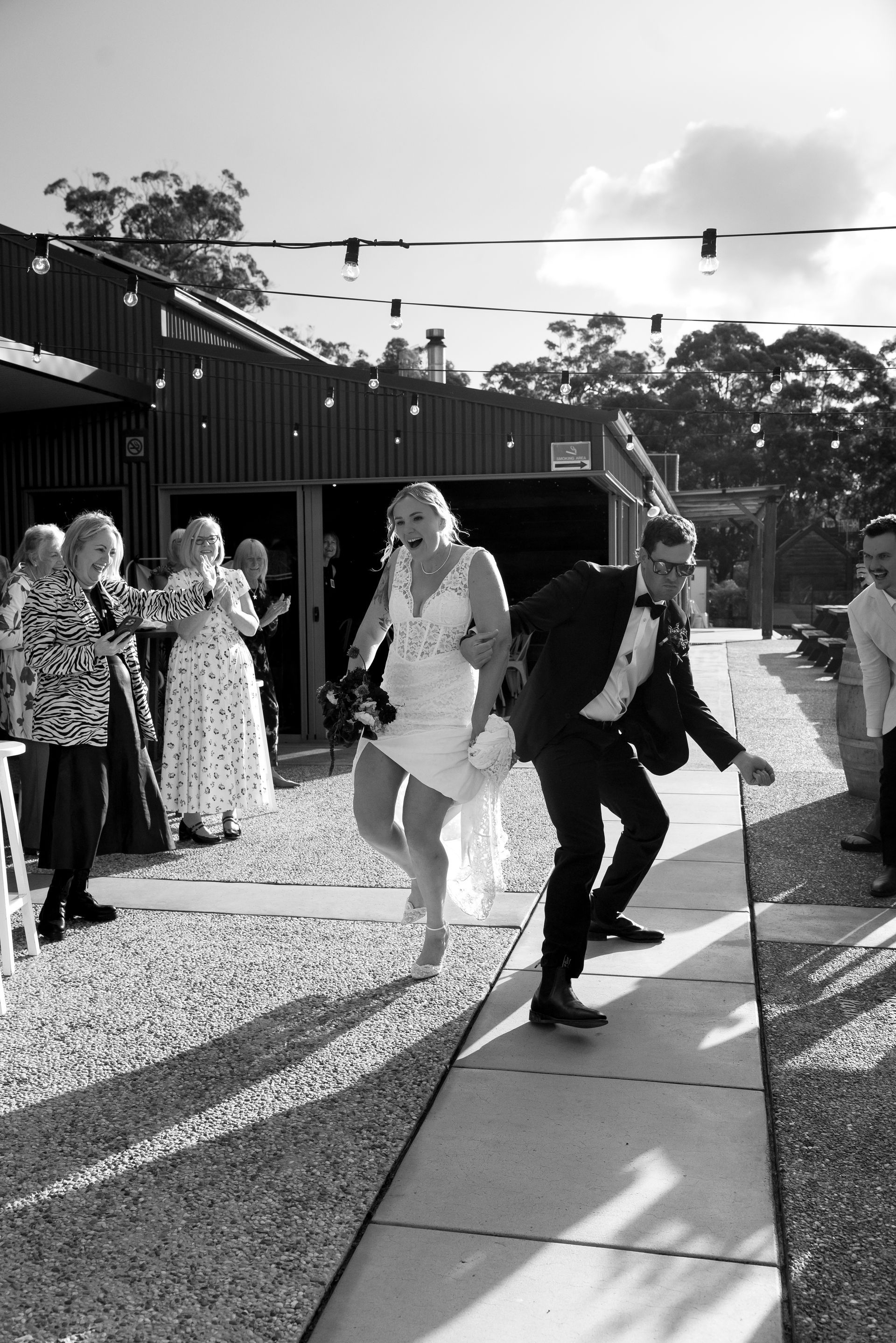 A Black and White Photo of A Bride and Groom With Sunglasses on Walking Through 2 Lines of People Holing Sparklers — Seed + Salt Photography In Smithtown, NSW