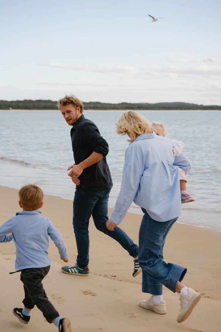 Two Adults and a Child Running Along a Sandy Beach Beside Calm Water โ Seed + Salt Photography In Smithtown, NSW