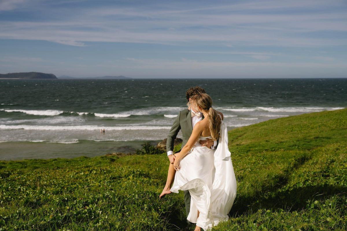 Couple in White Embraces on a Grassy Seaside Cliff โ Seed + Salt Photography In Smithtown, NSW