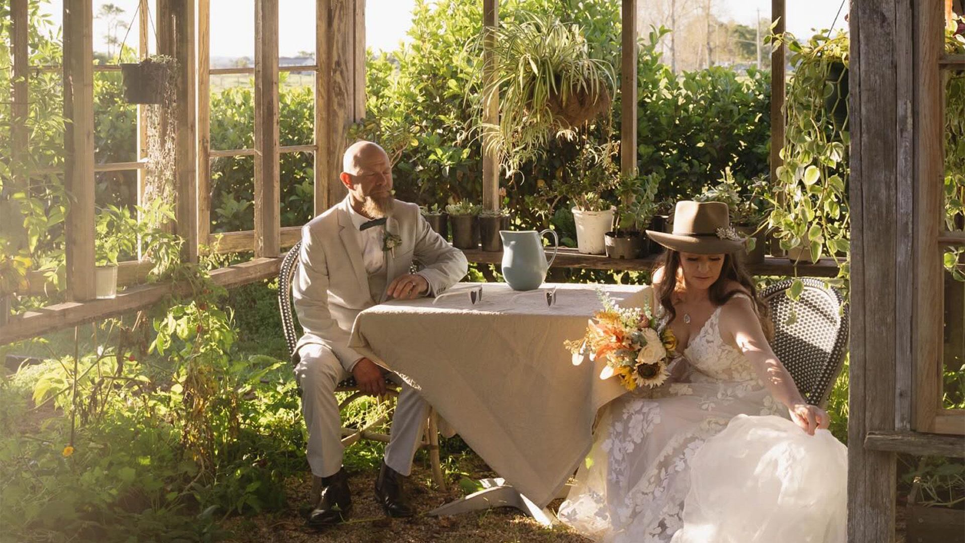 A Bride and Groom Are Sitting at A Table in A Greenhouse โ Seed + Salt Photography In Smithtown, NSW