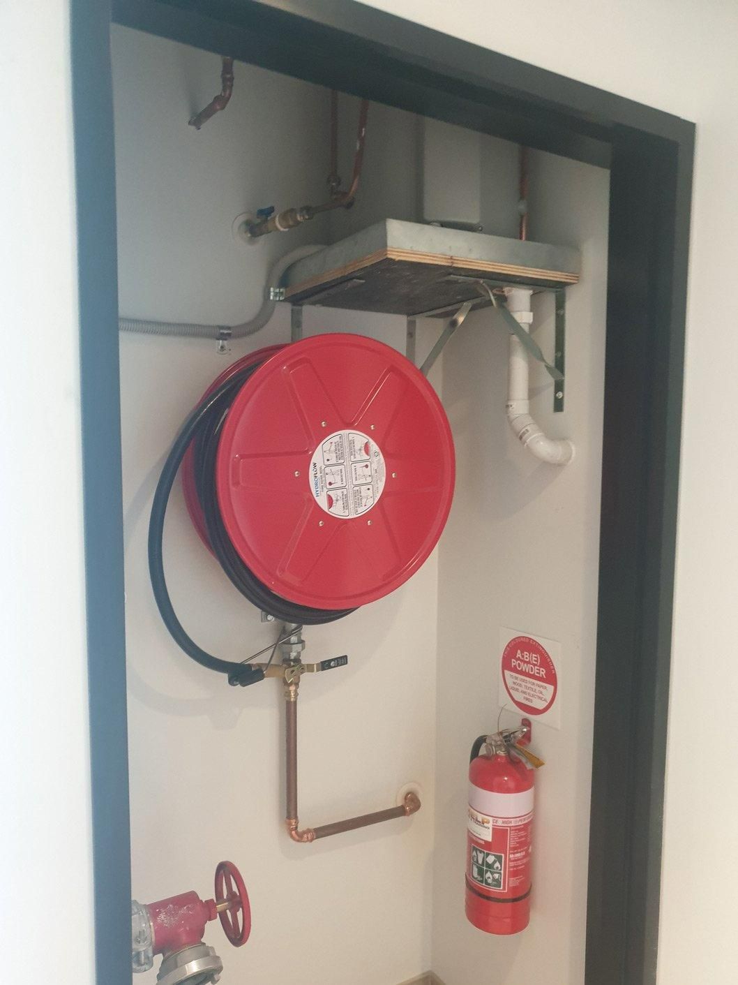 A Red Fire Hose Is Hanging on A Wall Next to A Fire Extinguisher — Gillespie Plumbing in Grafton, NSW