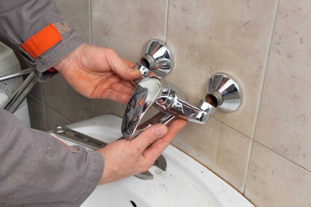 A Man Is Fixing a Faucet in A Bathroom — Gillespie Plumbing in Grafton, NSW