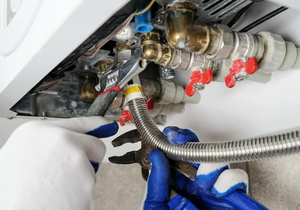 A Person Wearing Blue Gloves Is Working on A Water Heater — Gillespie Plumbing in Grafton, NSW