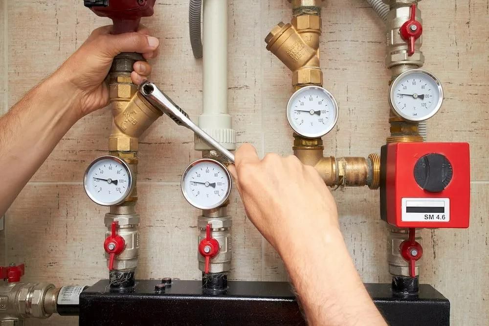 A Man Is Working on A Heating System with A Wrench — Gillespie Plumbing in Grafton, NSW