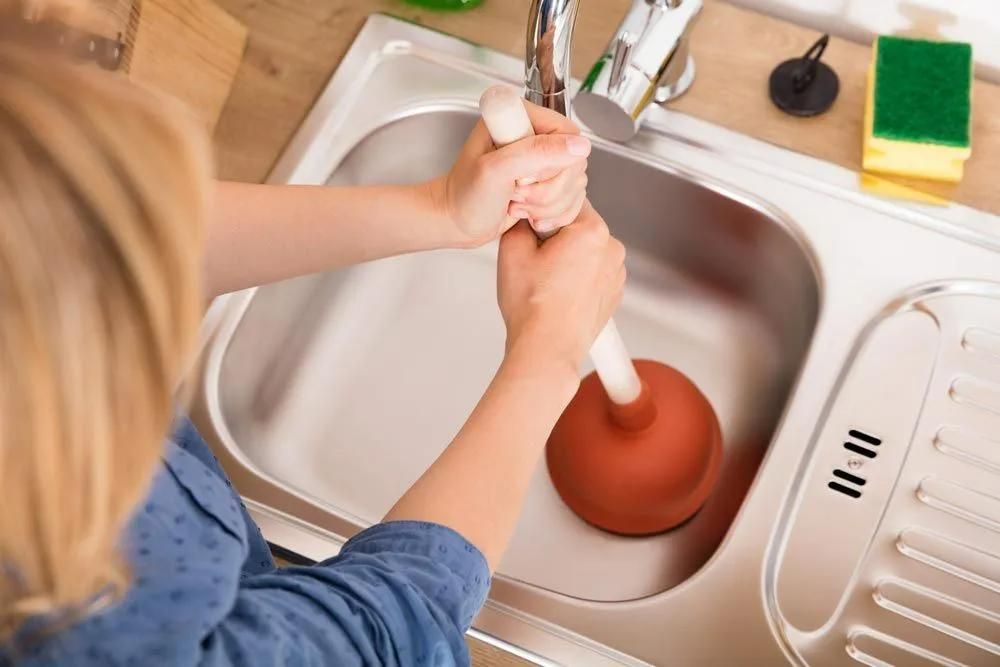 A Woman Is Using a Plunger to Unblock a Sink — Gillespie Plumbing in Grafton, NSW
