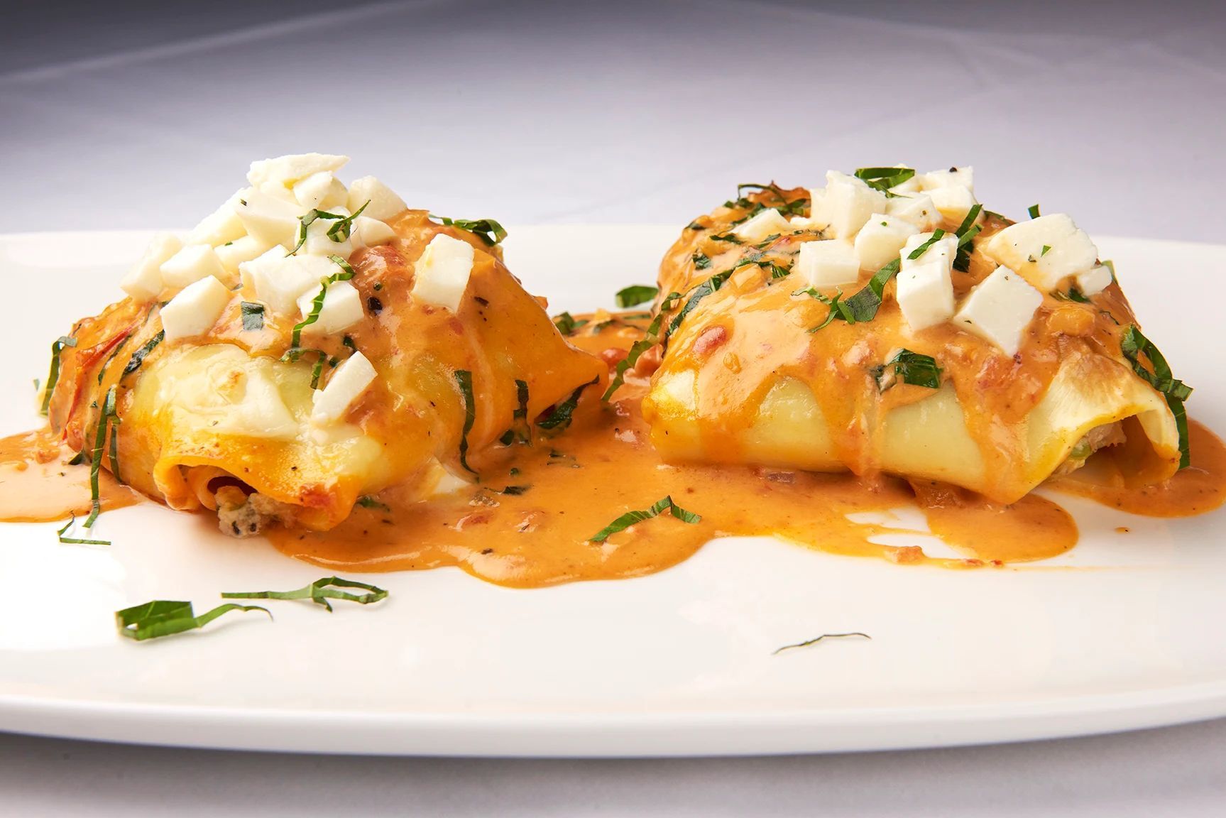 Two pieces of food on a white plate with sauce on top
