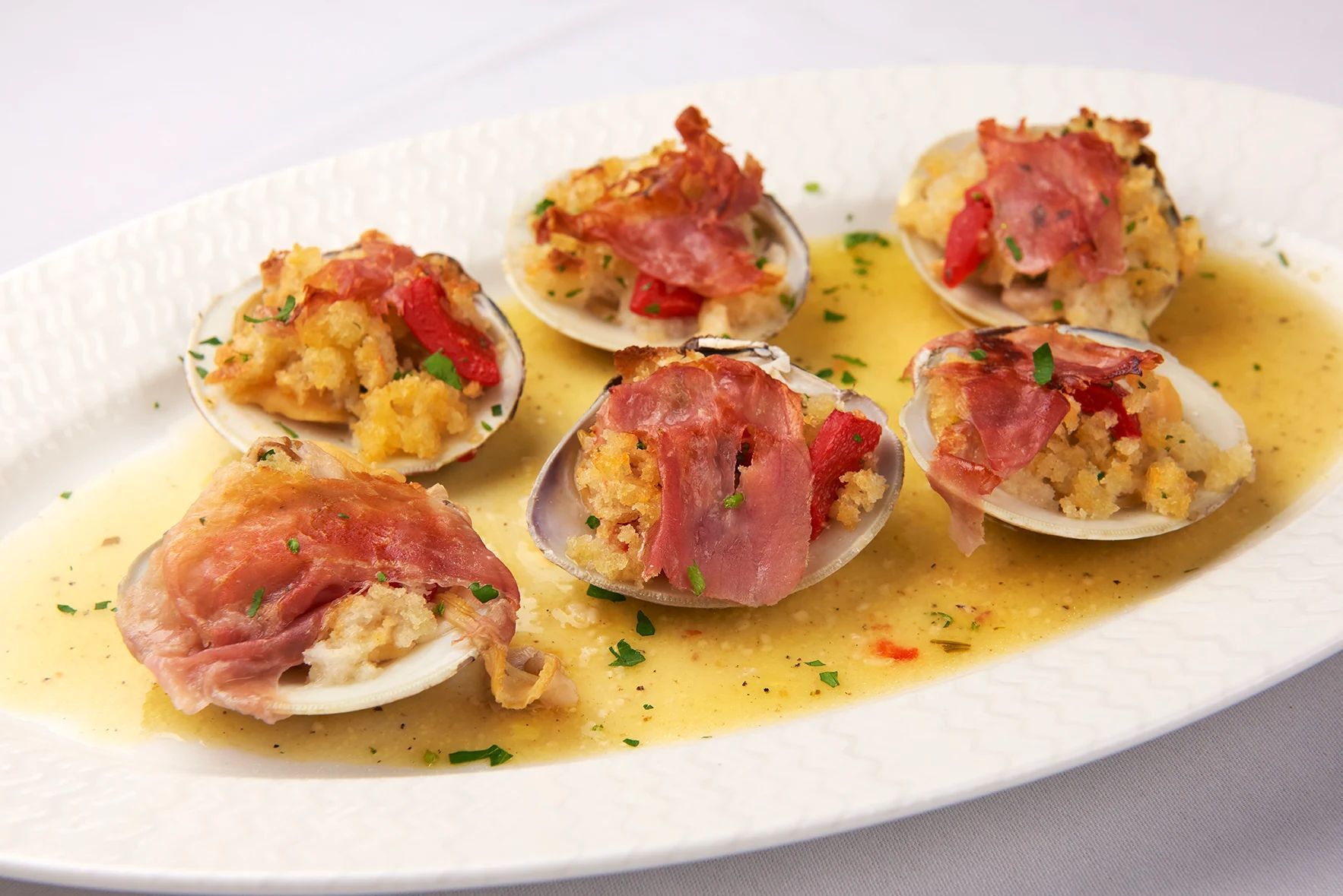 Clams San Danielle A white plate topped with clams and meat on a table.