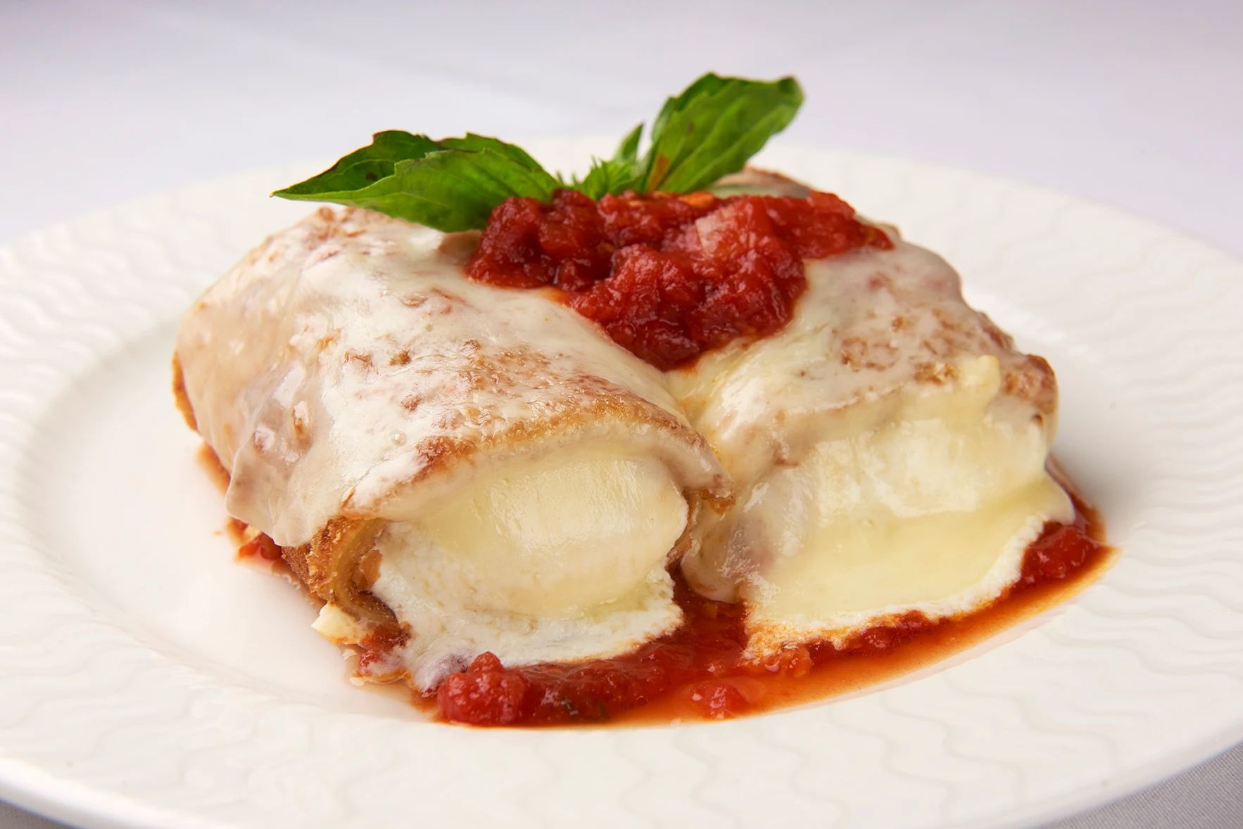 Eggplant Rollatini A white plate topped with a piece of food with tomato sauce and cheese.