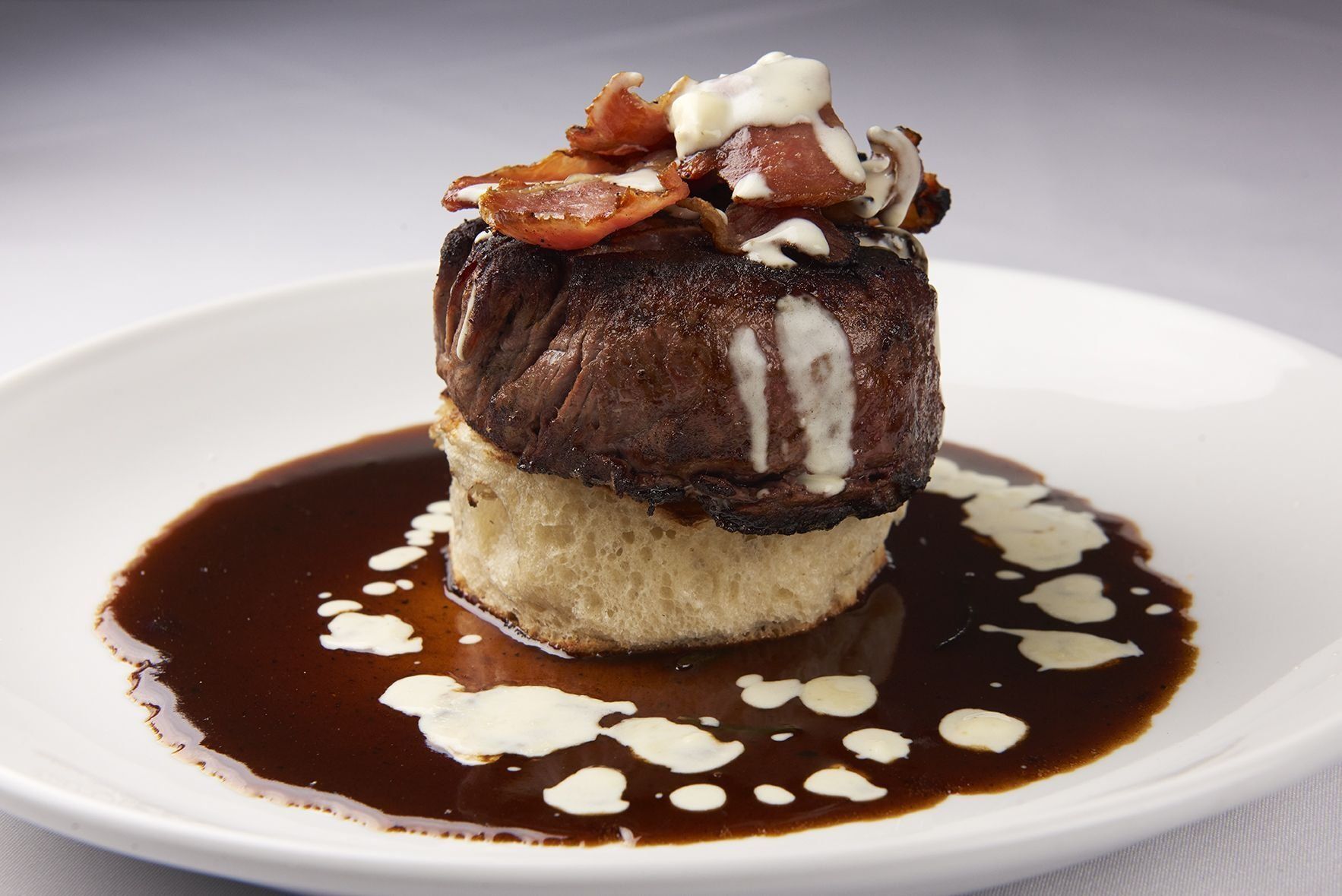 Filet Rossini E Gorgonzola Crema A white plate topped with a steak and sauce