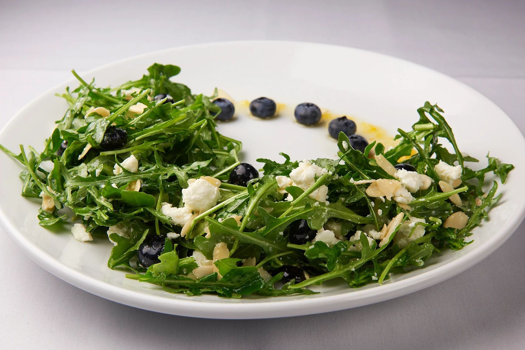 Baby Arugula Salad A white plate topped with a salad with blueberries and cheese.