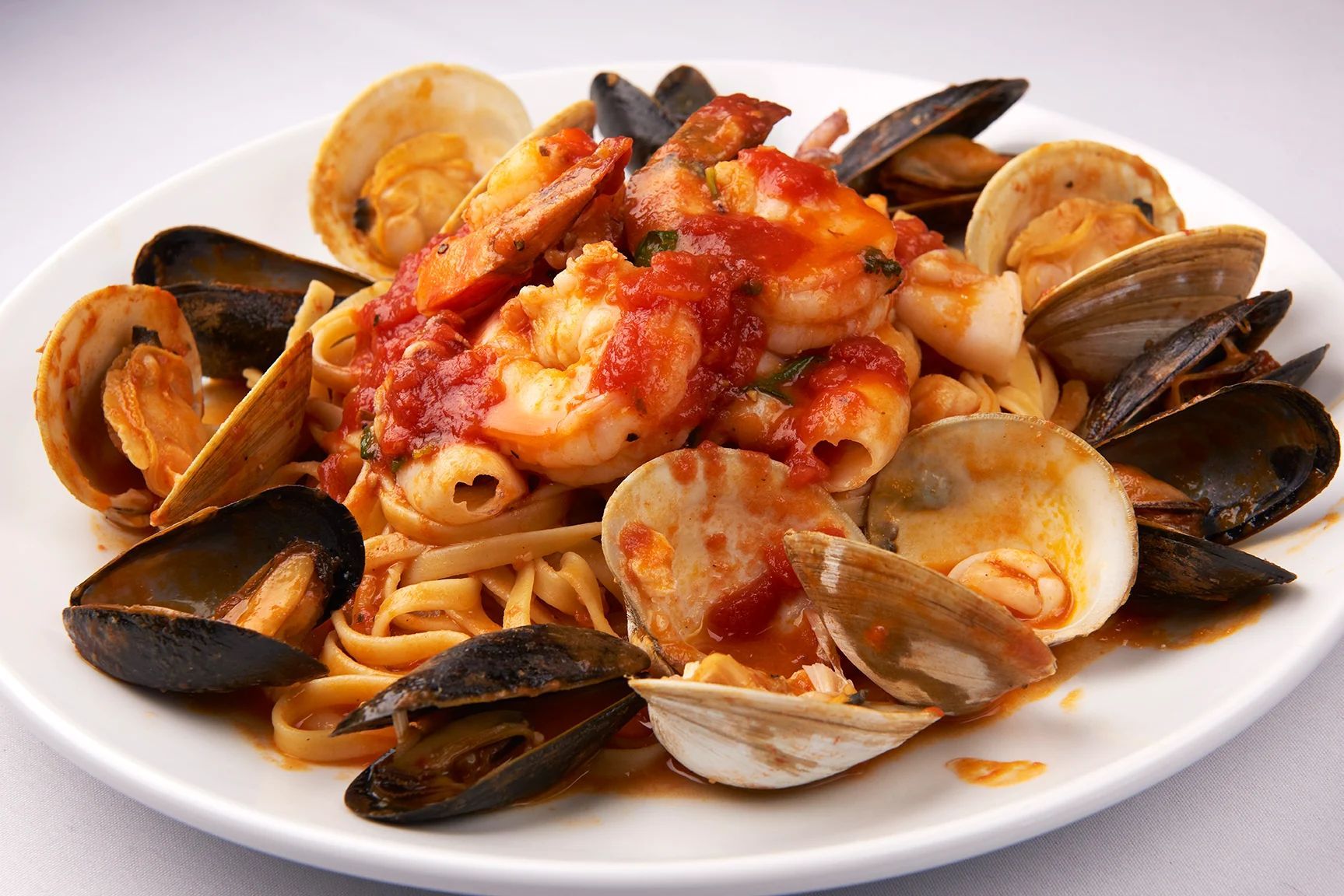 Frutta De Mare Fra Diavolo Or Marinara A white plate topped with noodles clams and shrimp
