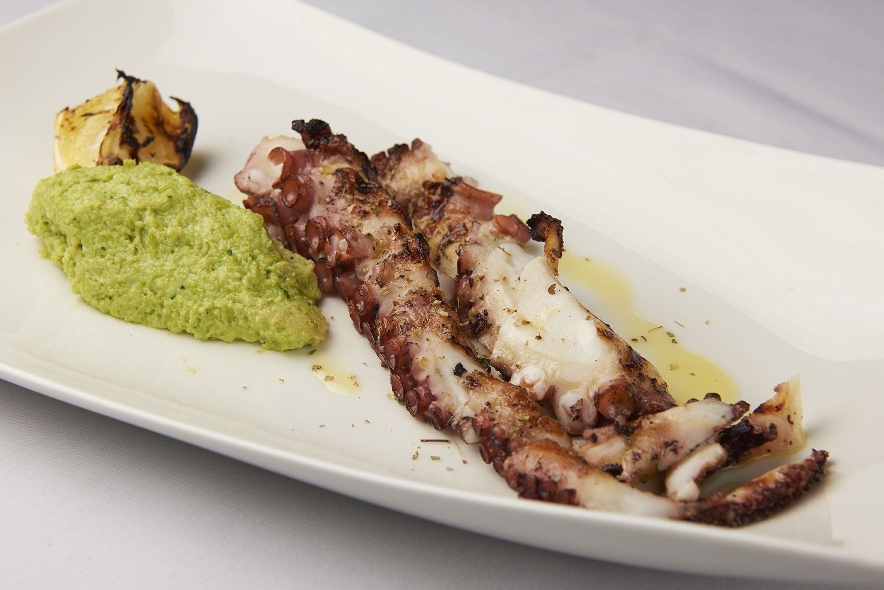 Grilled Octopus A white plate topped with grilled octopus and green sauce