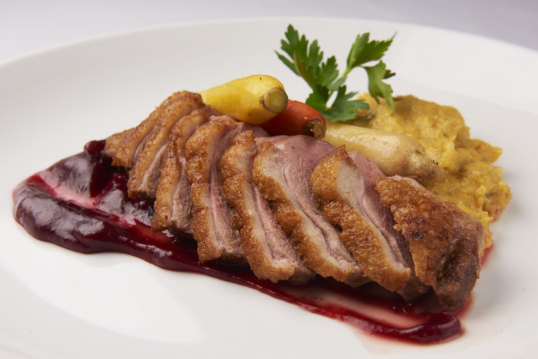 Hudson Valley Duck Breast A white plate topped with sliced meat and sauce