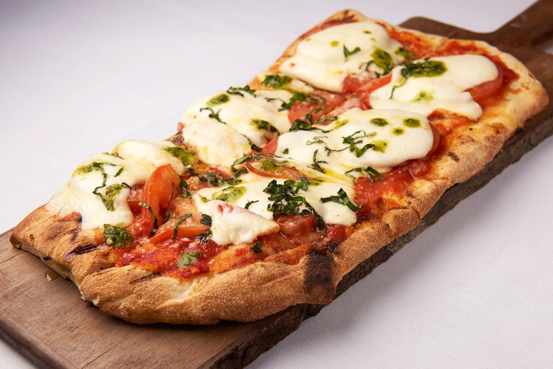 A pizza with tomatoes and cheese is on a wooden cutting board.