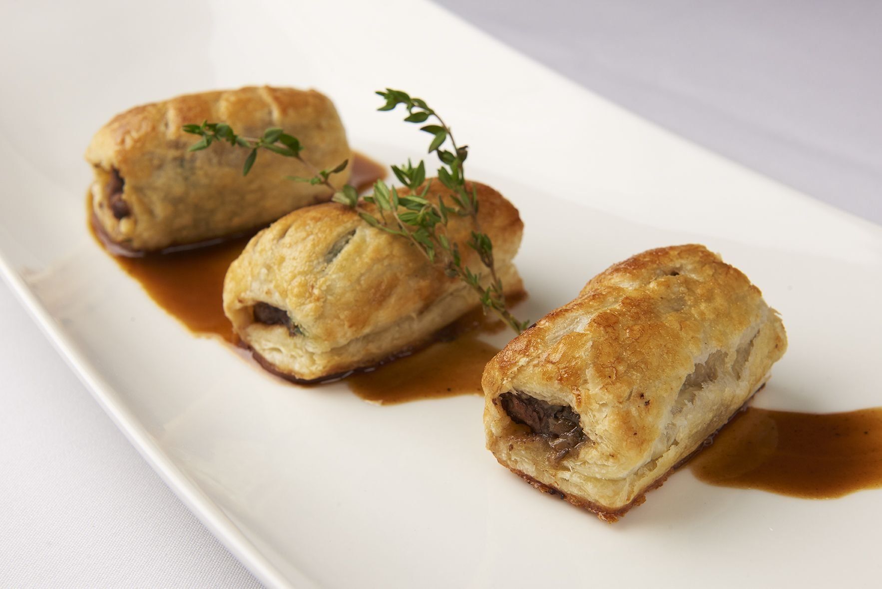 Mini Beef Wellington Three pastry rolls with sauce on a white plate