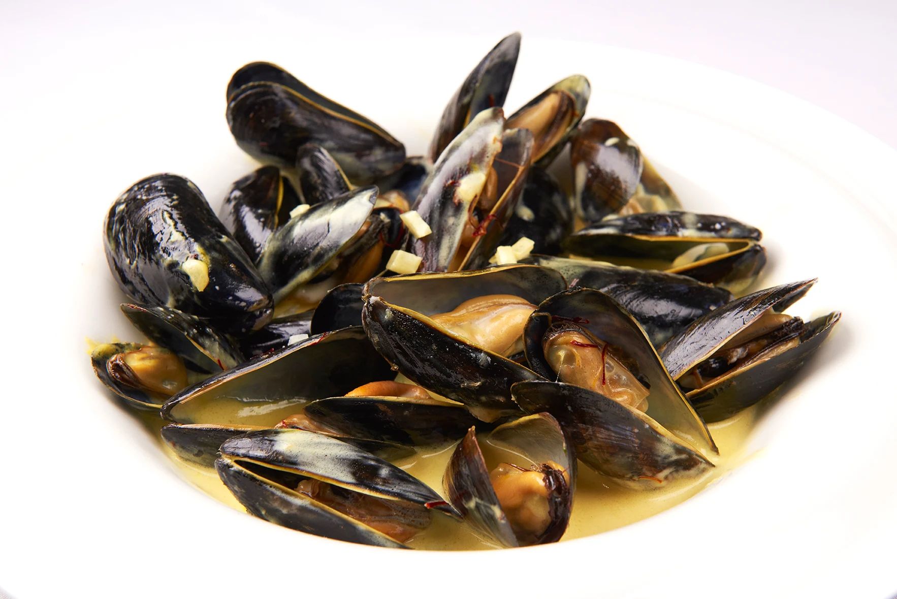 Mussels Saffronetta A white bowl filled with mussels in a sauce