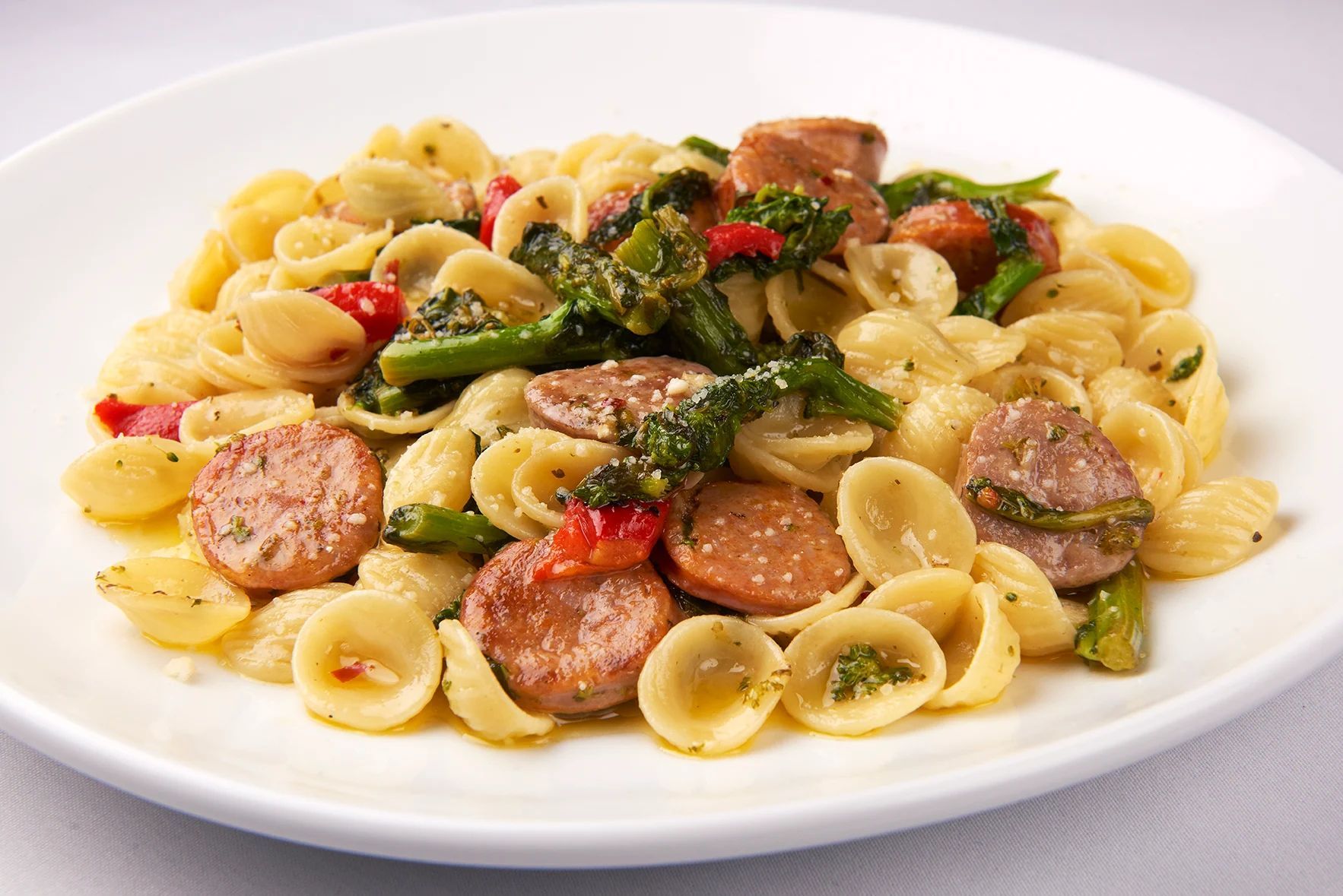 Orecchiette Baresse A white plate topped with pasta sausage and broccoli