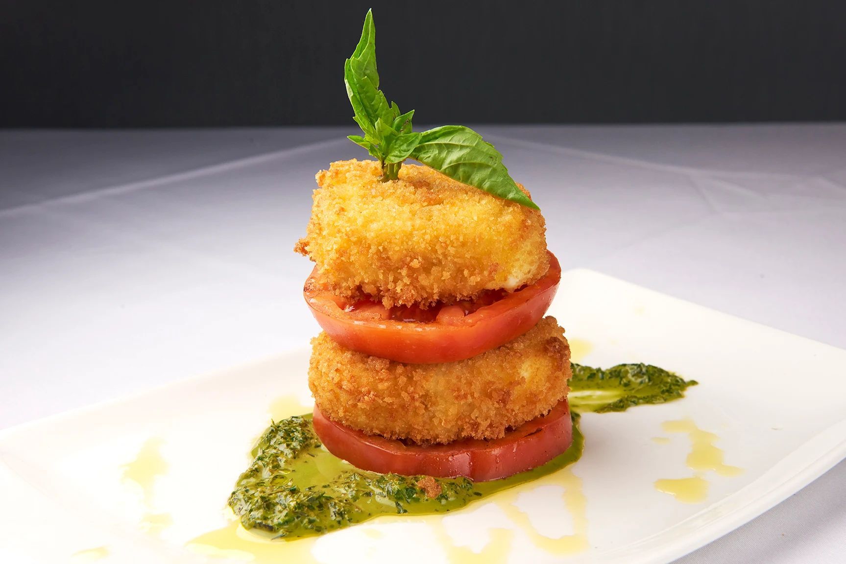 Panko Mozzarella Caprese A white plate topped with fried tomatoes and pesto sauce