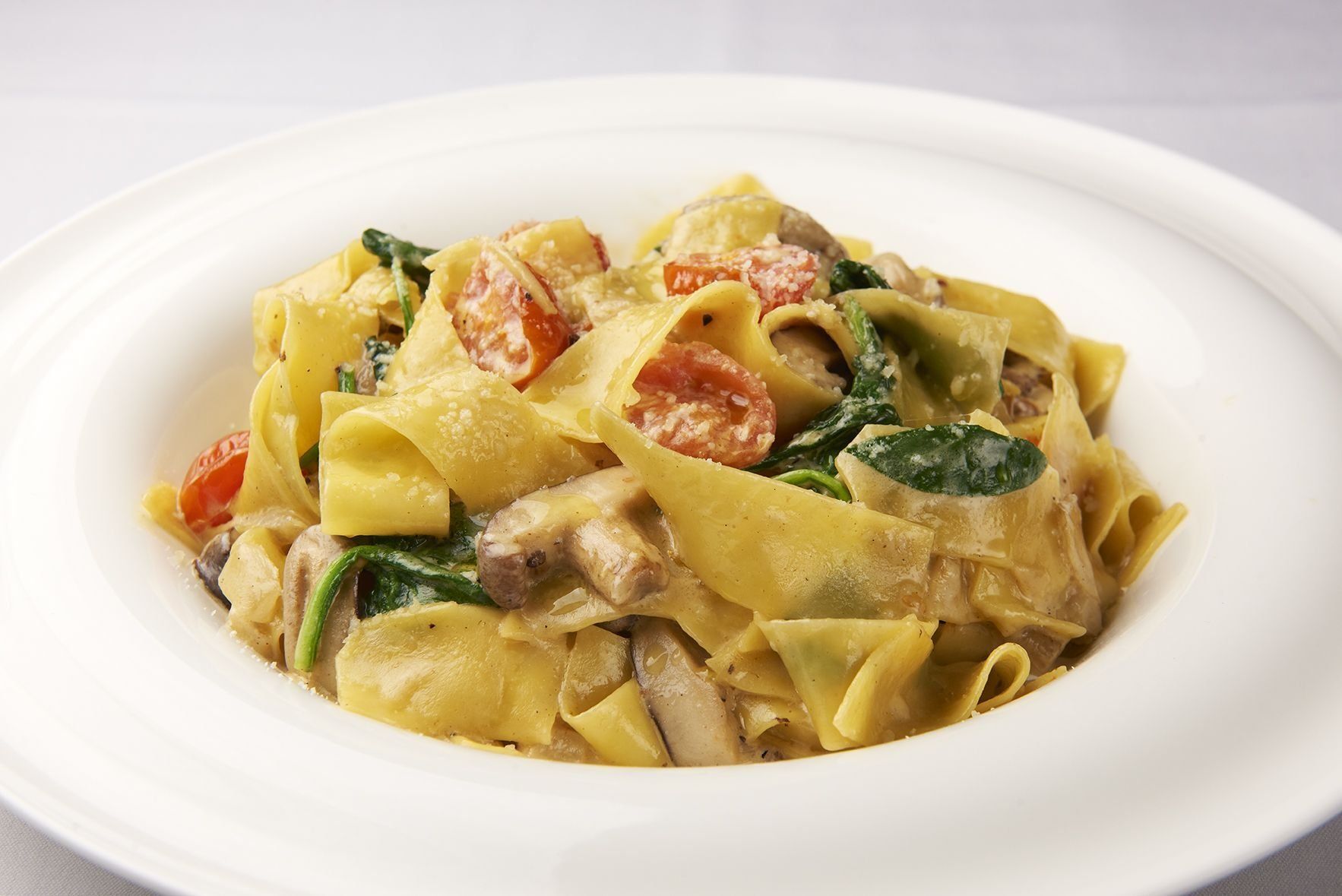 Pappardella Fresca A white plate topped with pasta tomatoes and spinach