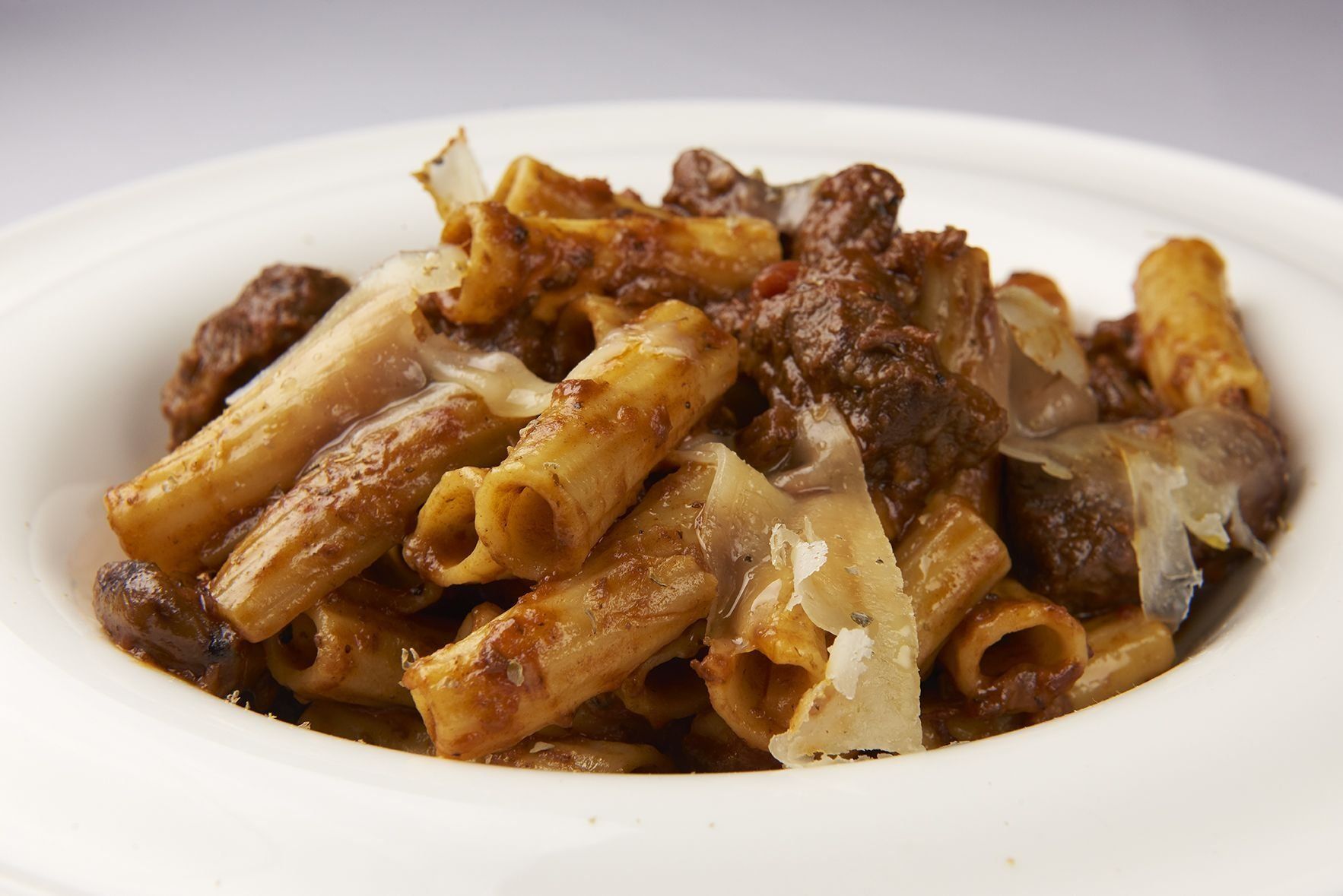 Rigatoni Agnello A white bowl filled with pasta and meat on a table.