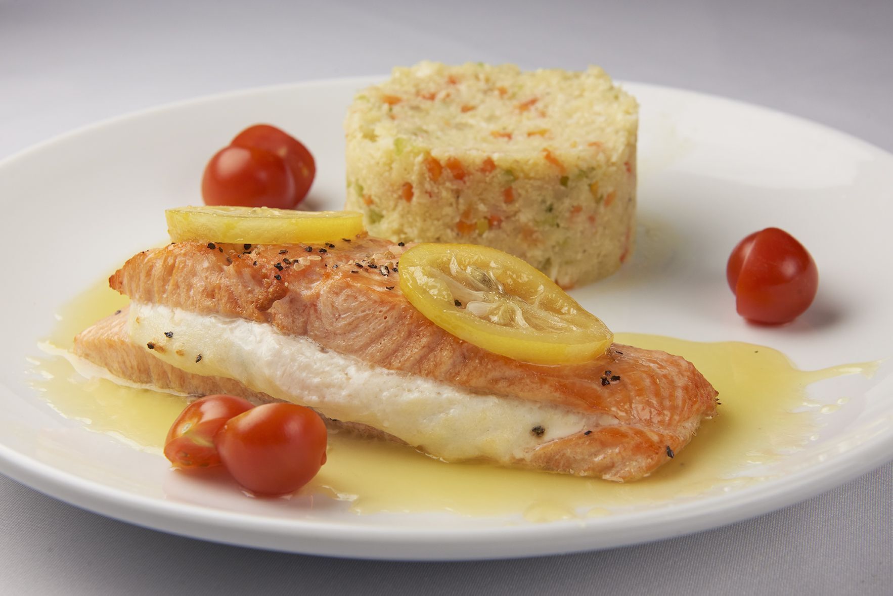 Salmon Limoncello A white plate topped with salmon , rice and tomatoes.