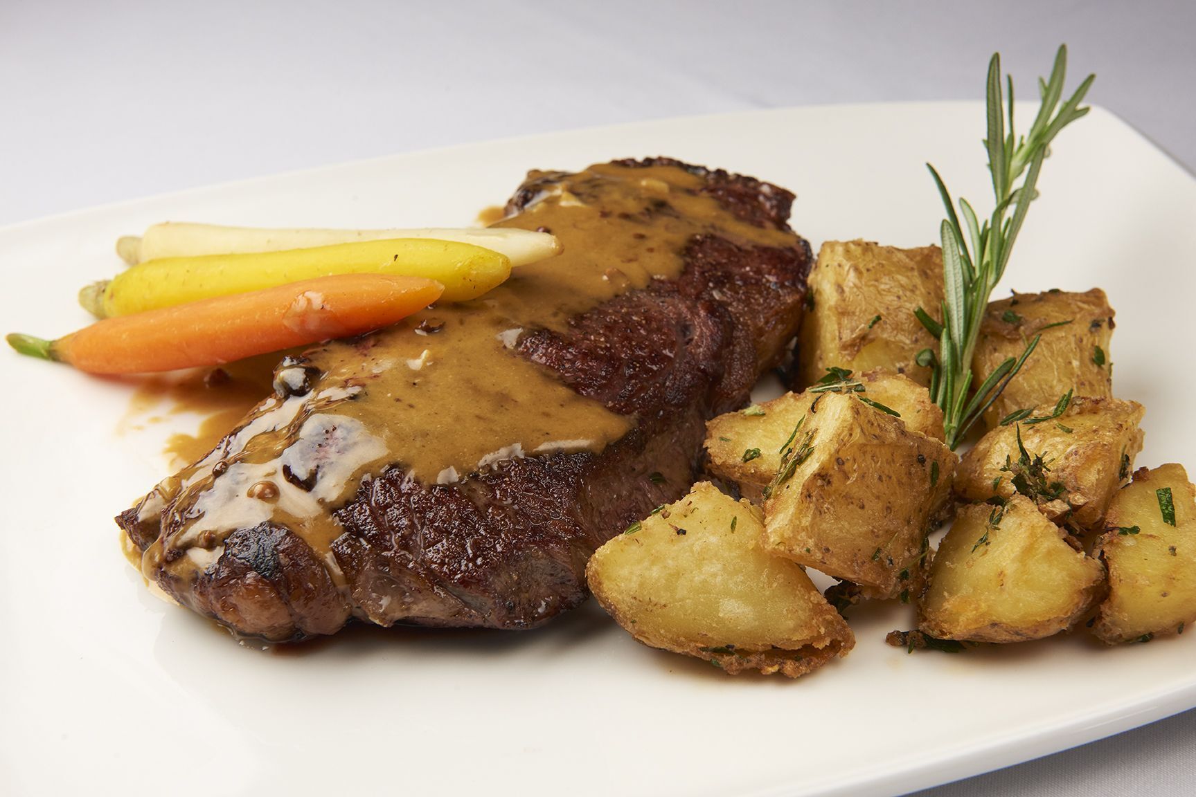 Steak Au Poivre A white plate topped with steak potatoes and carrots