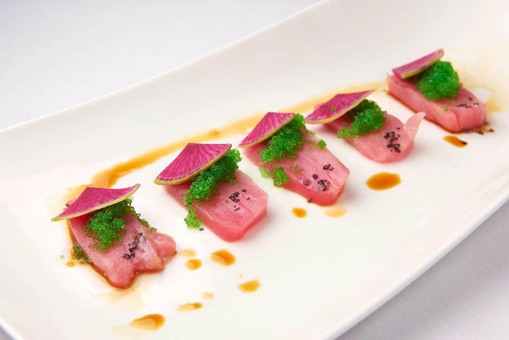 Sushi Grade Tuna With Caviar A white plate topped with meat and vegetables on a table.