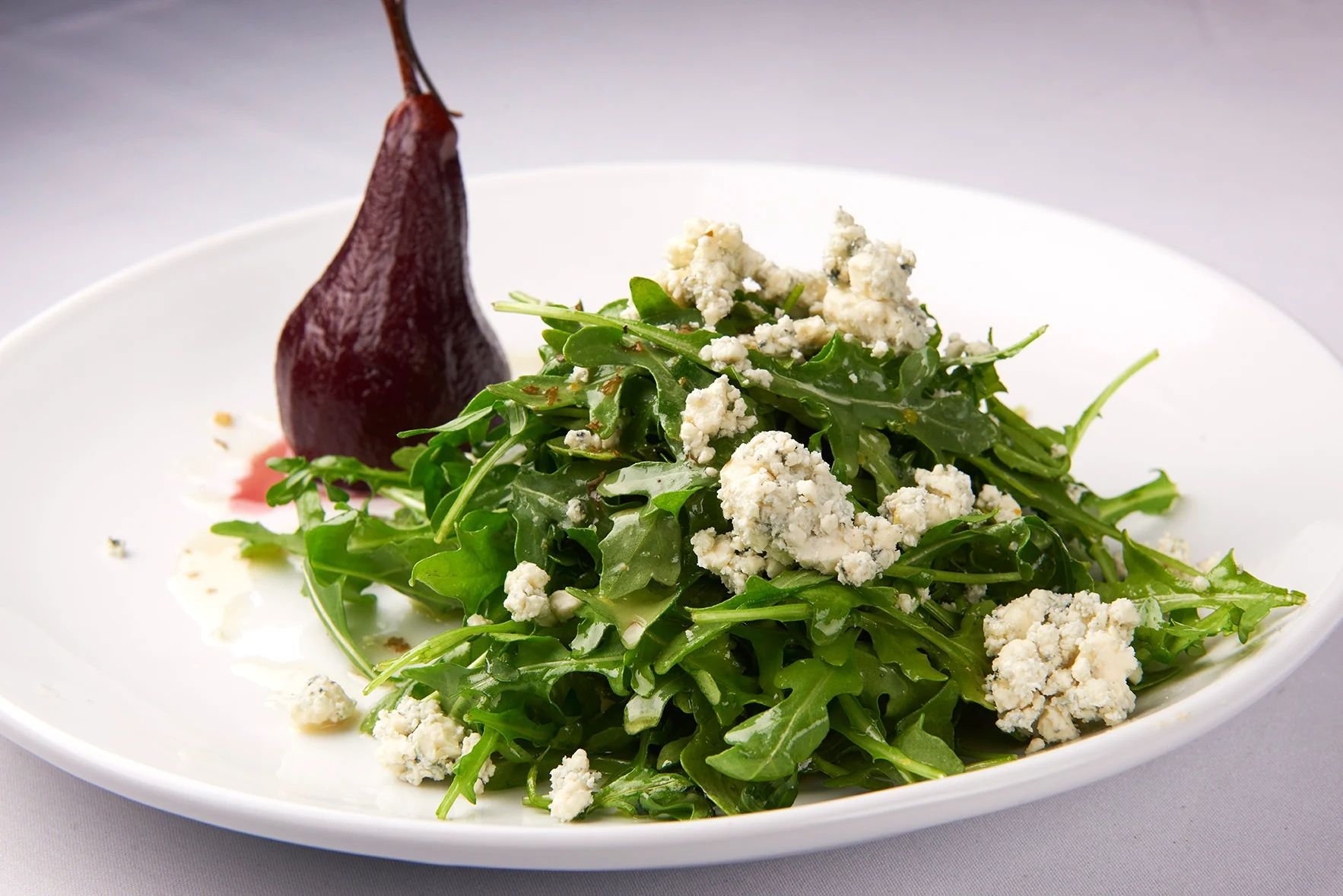 Blue Cheese & Poached Pear A white plate topped with a salad and a pear