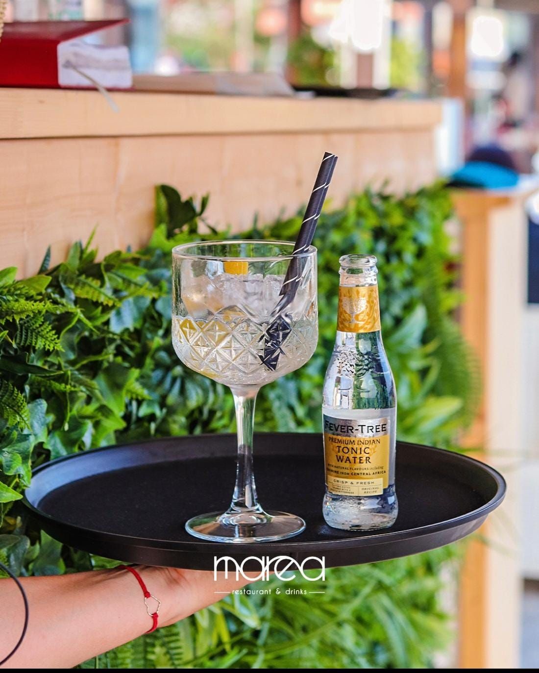 Una persona tiene in mano un vassoio con sopra un bicchiere e una bottiglia d'acqua.